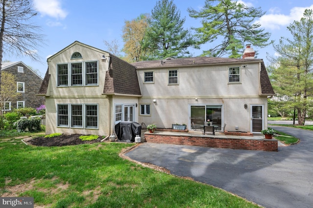 rear view of house featuring a chimney, a yard, a patio, a shingled roof, and stucco siding