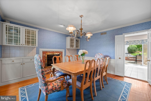 dining area featuring a notable chandelier, ornamental molding, light wood finished floors, and a wainscoted wall