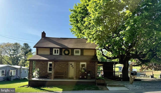 view of front facade featuring a porch, brick siding, a chimney, and roof with shingles