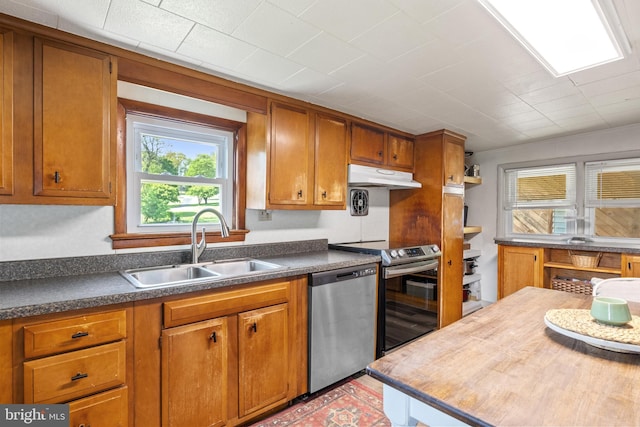 kitchen featuring brown cabinetry, a sink, under cabinet range hood, and stainless steel appliances