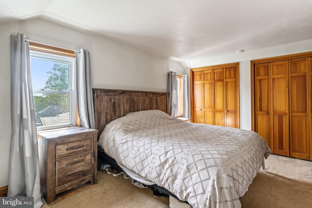 bedroom featuring light colored carpet, two closets, and vaulted ceiling