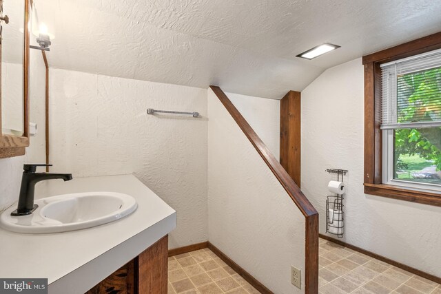 bathroom featuring a textured ceiling, vaulted ceiling, vanity, baseboards, and a textured wall