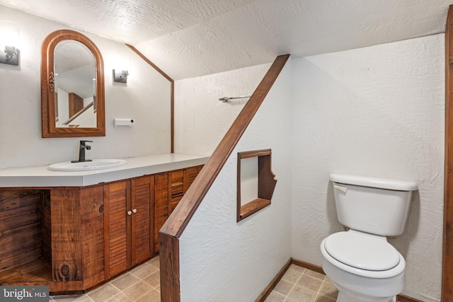 half bathroom with vanity, toilet, a textured ceiling, and lofted ceiling