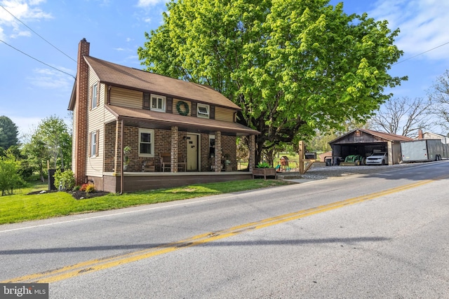 view of front facade featuring a detached carport, a front yard, a chimney, brick siding, and a porch