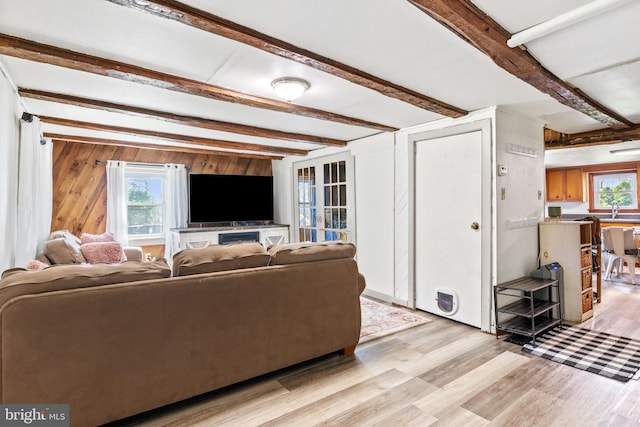 living room with wood walls, beam ceiling, and light wood-type flooring