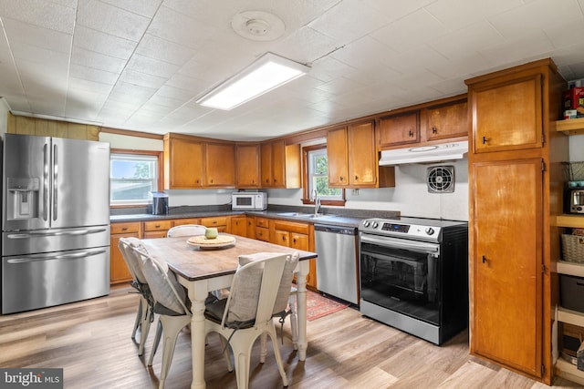 kitchen with under cabinet range hood, stainless steel appliances, brown cabinetry, and plenty of natural light