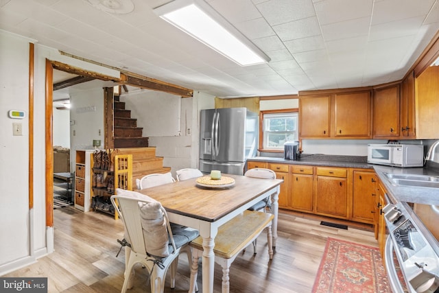 kitchen with dishwashing machine, brown cabinets, light wood-style flooring, and stainless steel fridge with ice dispenser