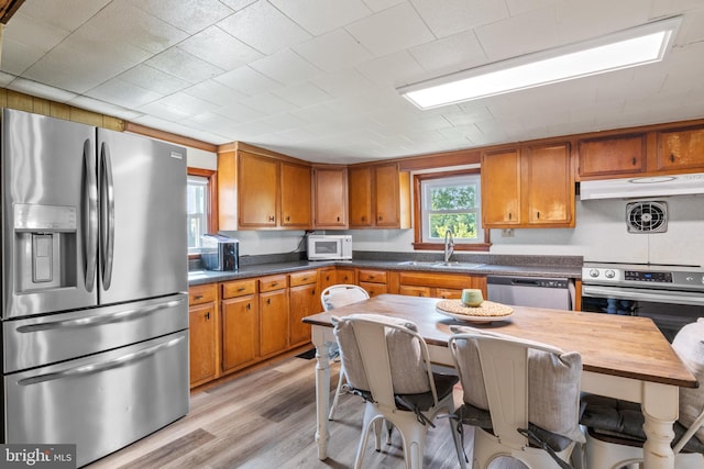 kitchen with a sink, stainless steel appliances, brown cabinets, and light wood-style flooring