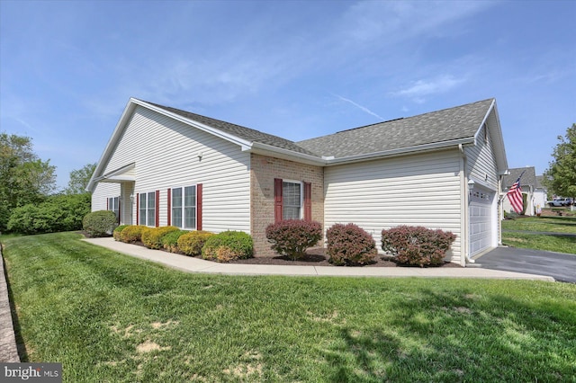 view of side of property featuring a lawn, a garage, brick siding, aphalt driveway, and a shingled roof