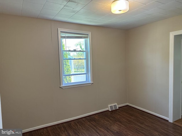 unfurnished room featuring baseboards, dark wood-type flooring, and visible vents
