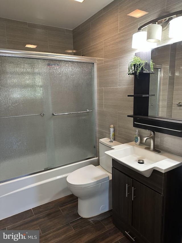 full bathroom with shower / bath combination with glass door, vanity, toilet, tile walls, and wood finished floors