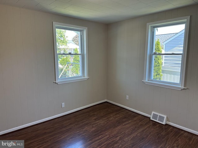 unfurnished room with visible vents, dark wood finished floors, and baseboards