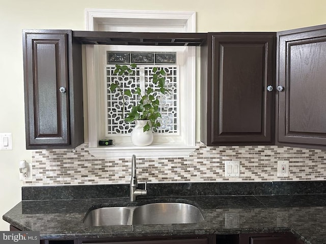 kitchen featuring a sink, dark stone counters, tasteful backsplash, and dark brown cabinets
