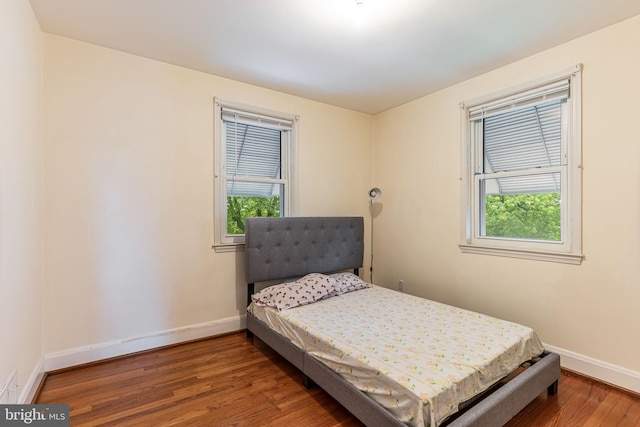 bedroom with baseboards, wood finished floors, and multiple windows