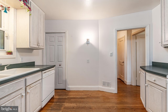kitchen featuring white dishwasher, wood finished floors, dark countertops, a sink, and baseboards