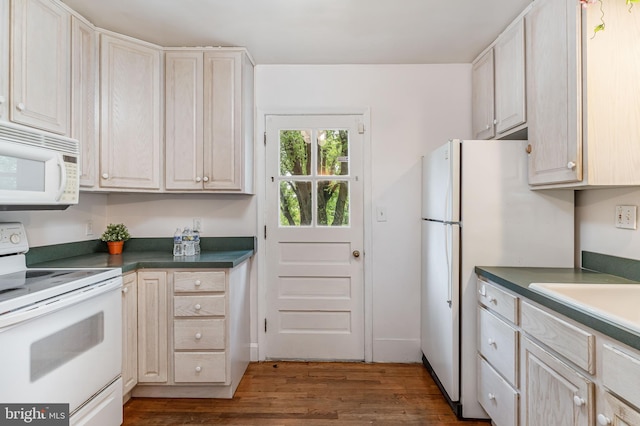 kitchen with white appliances, dark wood-type flooring, dark countertops, and a sink
