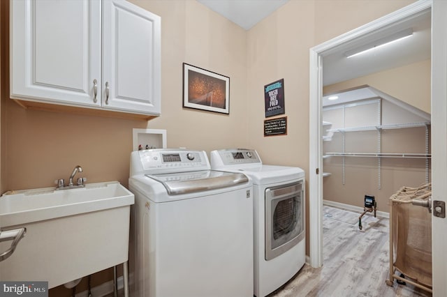 clothes washing area featuring a sink, washing machine and dryer, cabinet space, and light wood-style flooring