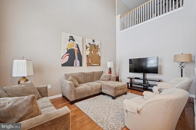 living area featuring a towering ceiling, wood finished floors, and baseboards