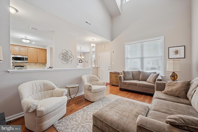 living area with an inviting chandelier, baseboards, wood finished floors, and visible vents