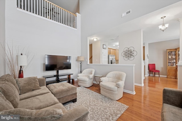 living area featuring a notable chandelier, light wood-type flooring, visible vents, baseboards, and a towering ceiling