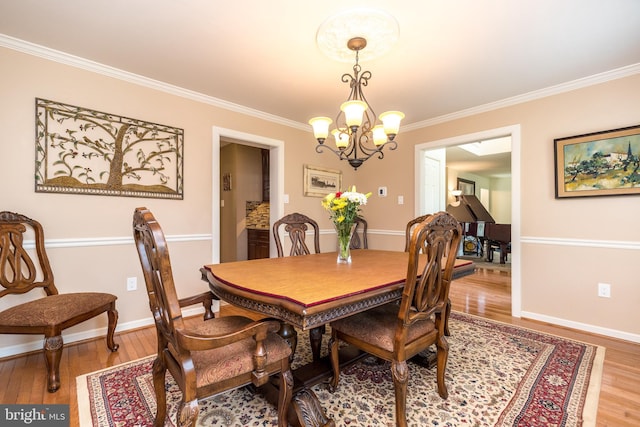 dining room featuring crown molding, baseboards, a chandelier, and light wood-type flooring