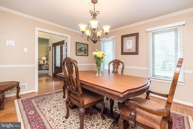 dining space with a notable chandelier, ornamental molding, and light wood-style floors