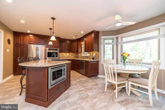 kitchen with decorative backsplash, a ceiling fan, a kitchen bar, appliances with stainless steel finishes, and light stone countertops