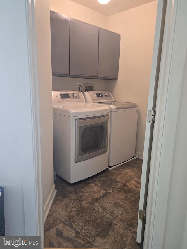 clothes washing area with stone finish flooring, cabinet space, and washing machine and clothes dryer
