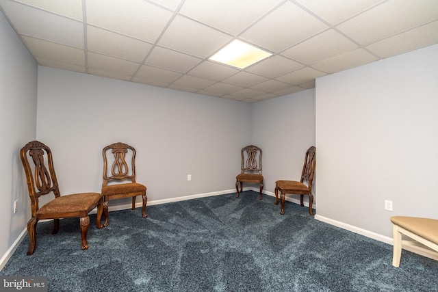 living area featuring baseboards, a drop ceiling, and dark carpet