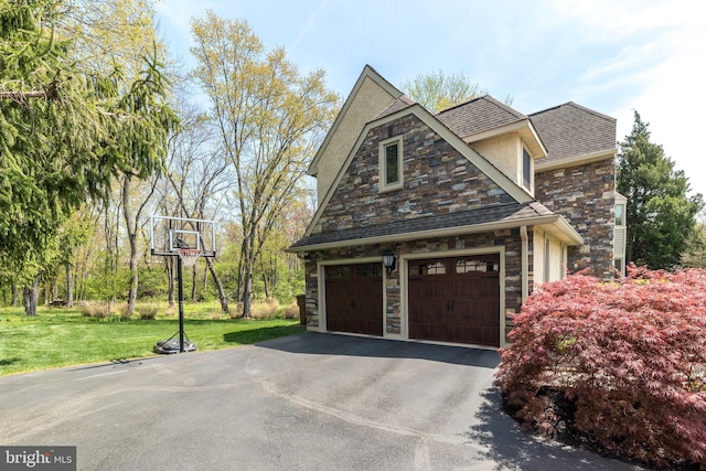 view of side of home with driveway, roof with shingles, a garage, a yard, and stone siding