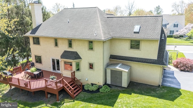 rear view of house with a chimney, roof with shingles, a lawn, a wooden deck, and stucco siding