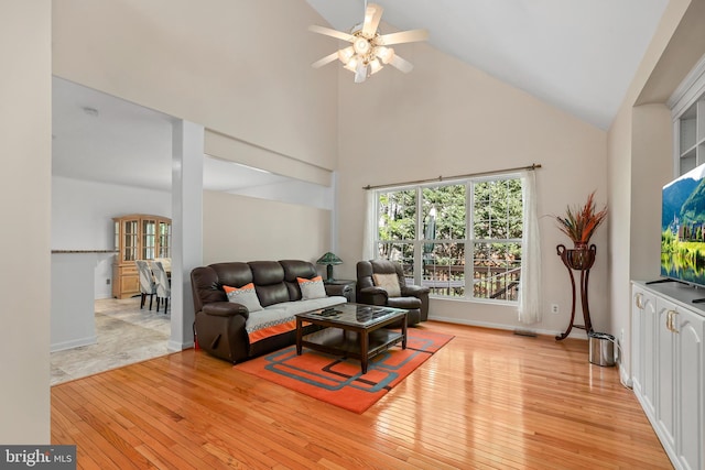 living area with a ceiling fan, high vaulted ceiling, baseboards, and light wood-type flooring