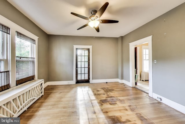 unfurnished room featuring plenty of natural light, a ceiling fan, radiator, and light wood finished floors