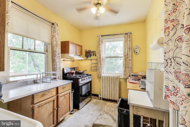 kitchen with brown cabinets, radiator, a ceiling fan, gas range, and under cabinet range hood