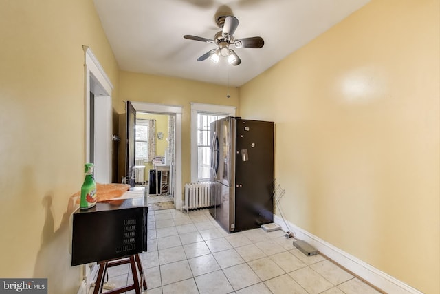 interior space featuring ceiling fan, radiator heating unit, freestanding refrigerator, baseboards, and light tile patterned floors