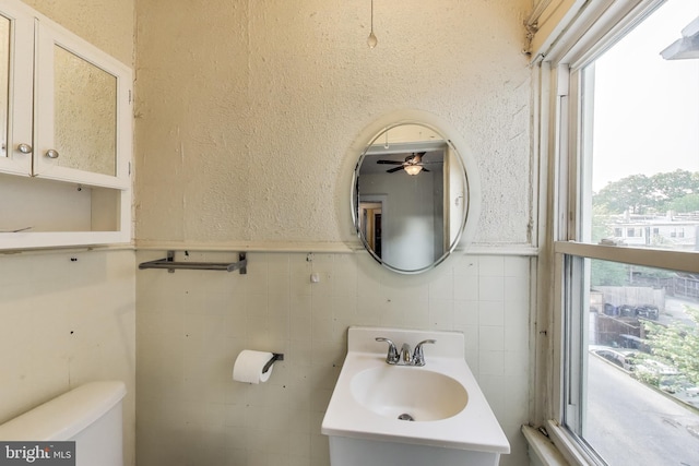 half bath with a sink, ceiling fan, toilet, and tile walls