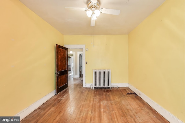 unfurnished room featuring wood-type flooring, a ceiling fan, baseboards, and radiator heating unit