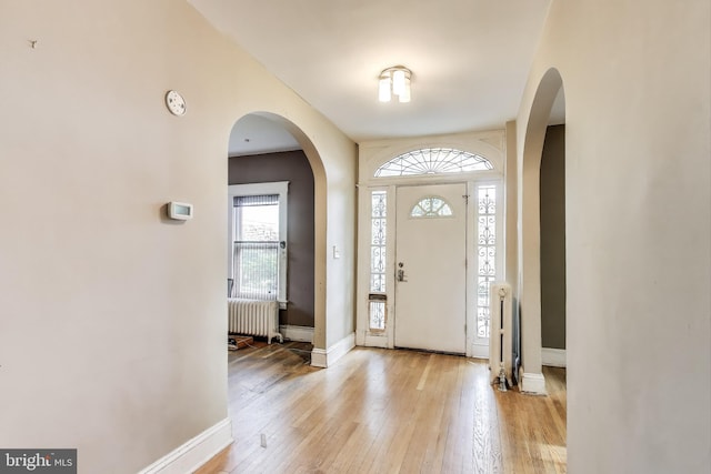 entryway with radiator, baseboards, arched walkways, and light wood-style flooring