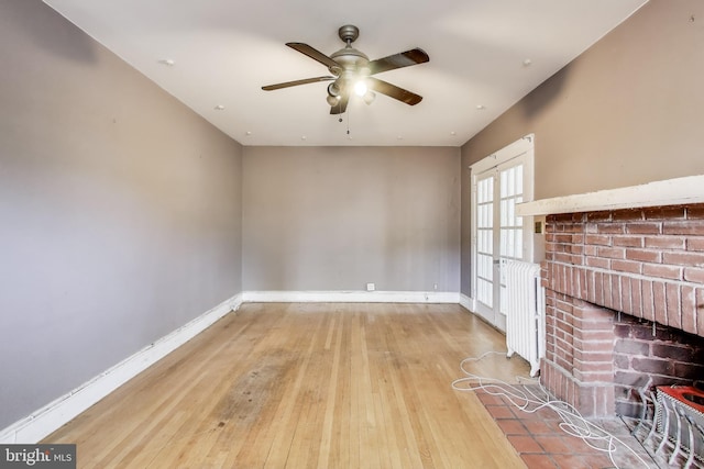 unfurnished living room with baseboards, ceiling fan, radiator heating unit, and hardwood / wood-style floors