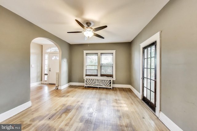 interior space with arched walkways, light wood-style flooring, ceiling fan, and a healthy amount of sunlight