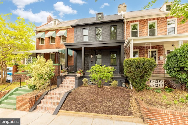 view of front facade featuring covered porch, brick siding, and a chimney