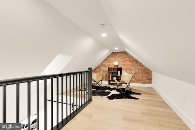 bonus room featuring brick wall, baseboards, vaulted ceiling, and wood finished floors