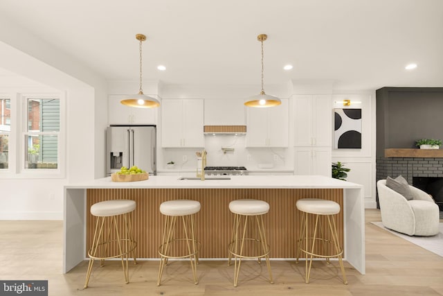kitchen featuring stainless steel refrigerator with ice dispenser, light countertops, white cabinets, a large island with sink, and a sink