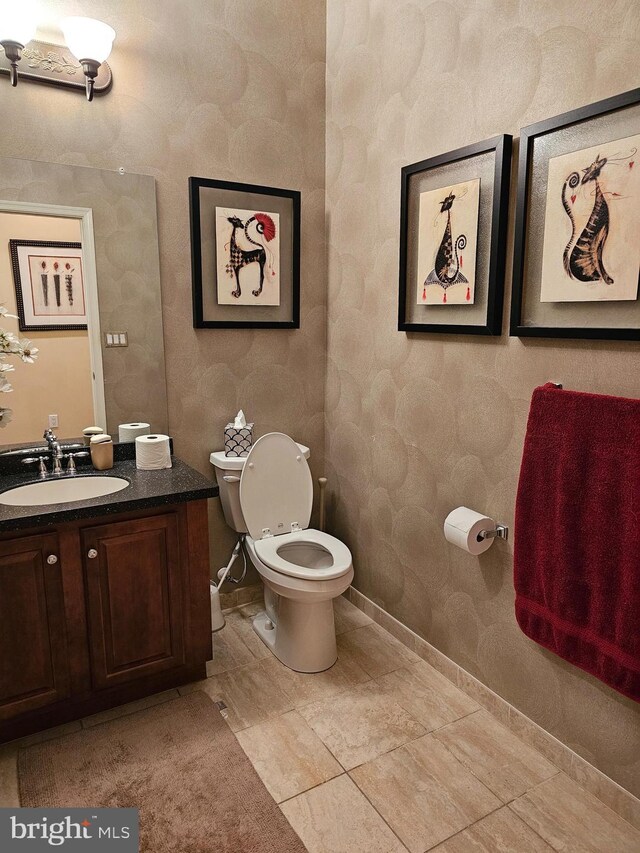 bathroom with baseboards, wallpapered walls, toilet, and vanity