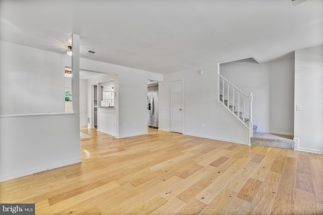 unfurnished living room featuring baseboards, visible vents, wood finished floors, and stairway