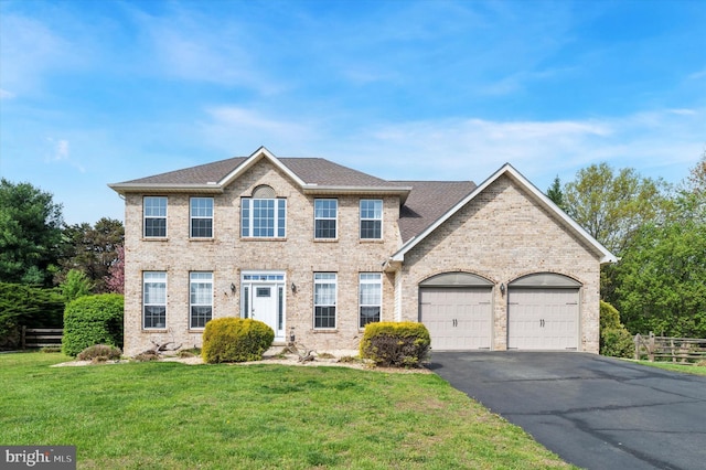 colonial inspired home with fence, an attached garage, brick siding, a front yard, and driveway