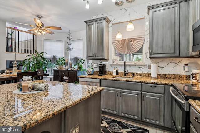 kitchen with ceiling fan, decorative backsplash, appliances with stainless steel finishes, a sink, and light stone counters