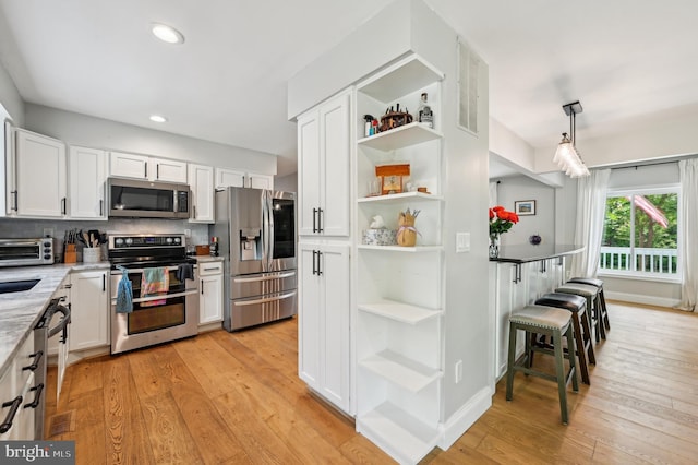 kitchen with open shelves, appliances with stainless steel finishes, light wood-type flooring, and white cabinetry
