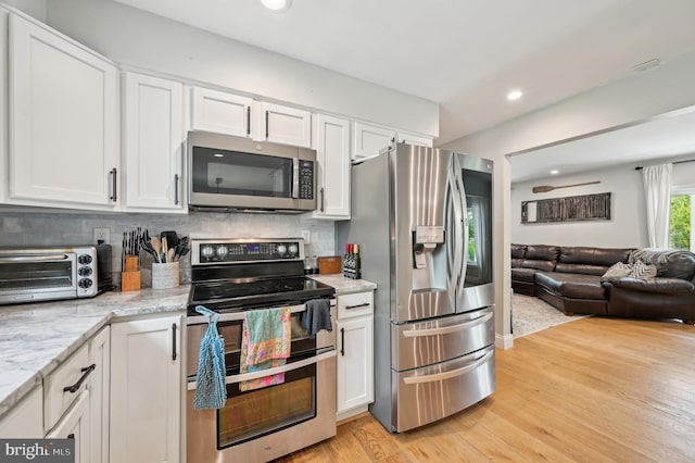 kitchen with a toaster, light wood finished floors, white cabinetry, open floor plan, and stainless steel appliances