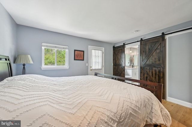 bedroom featuring wood finished floors, ensuite bathroom, a barn door, and baseboards